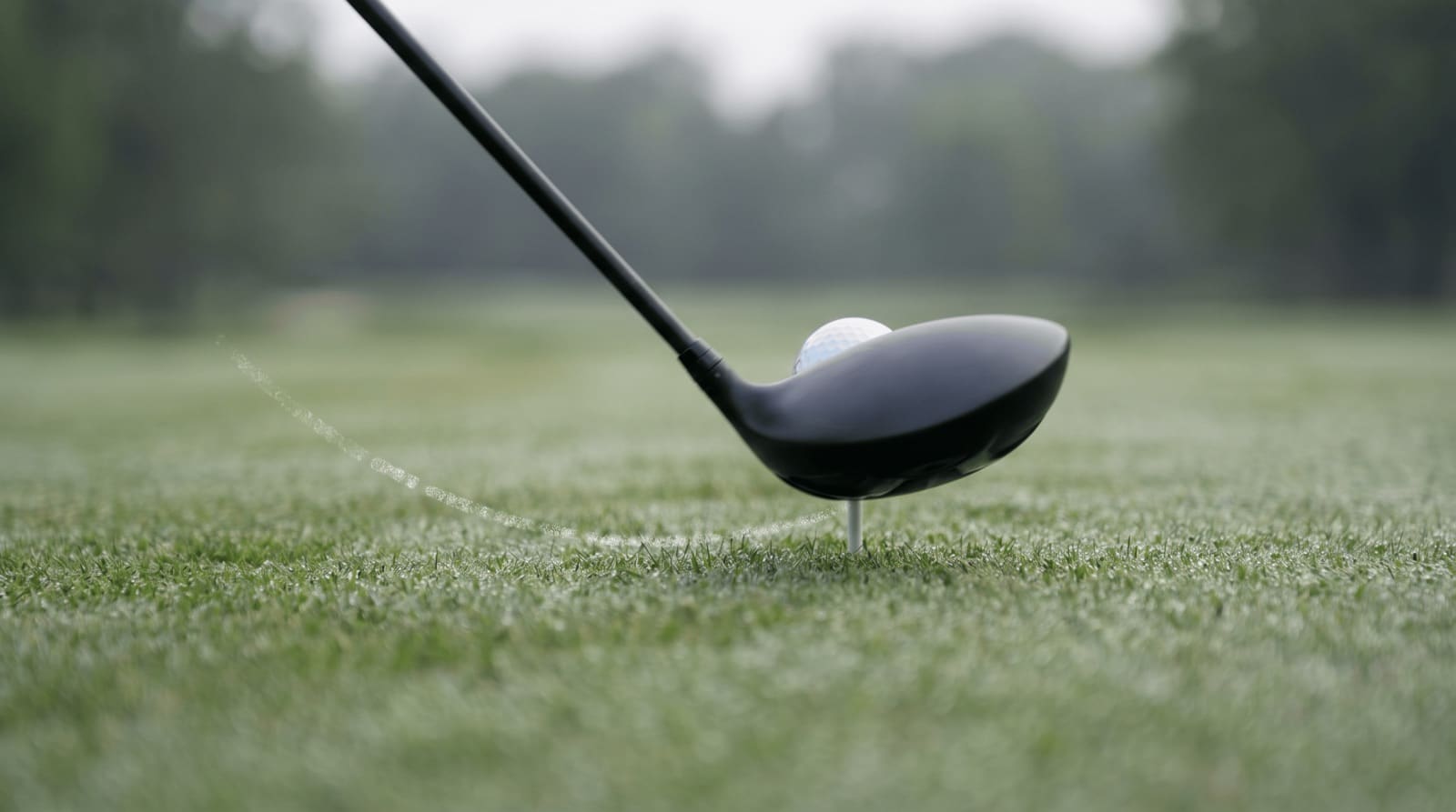 A driver catching a teed ball on the upswing, the clubhead ascending through a ball played off the lead heel with the shaft leaning slightly away from the target, the positive angle of attack that maximizes driver distance.